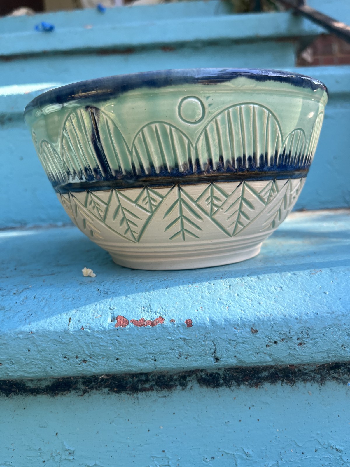 A carved blue and green bowl in sunlight on blue steps